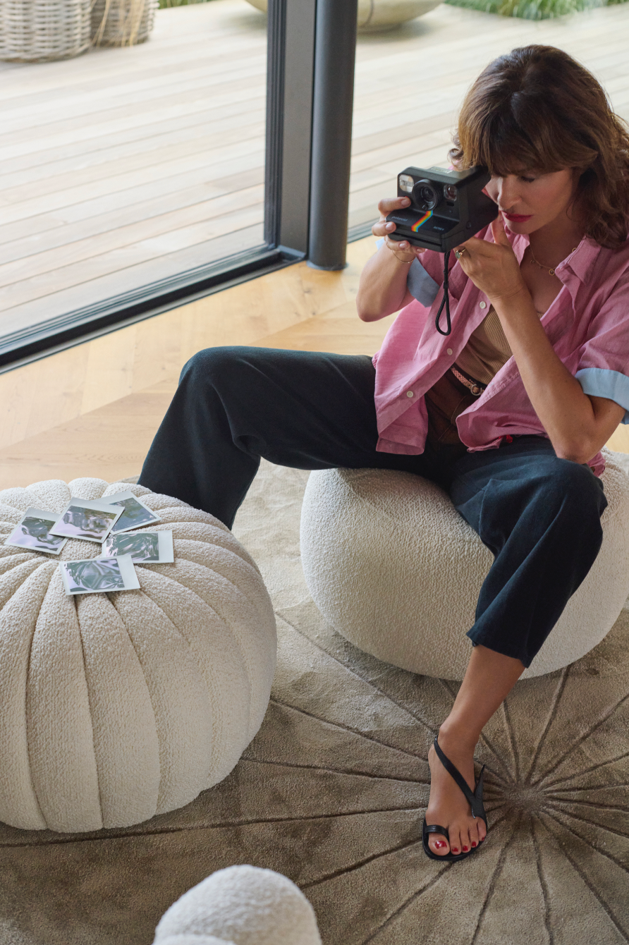 person taking a photograph with a camera sitting on a plush ottoman
