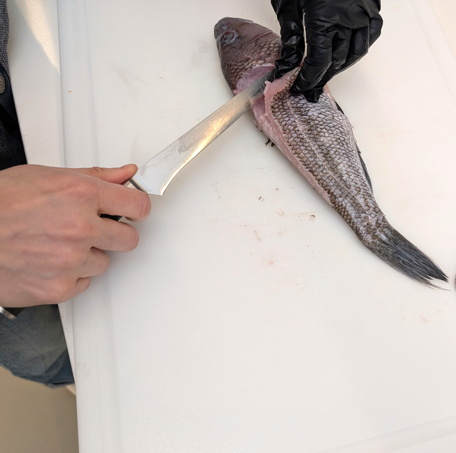 filleting a fish with a knife on a cutting board