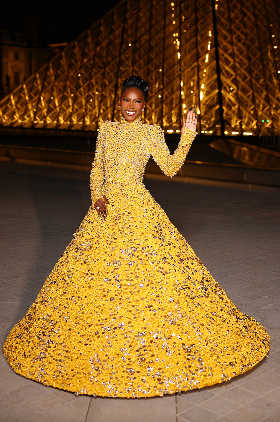 a person in a stunning yellow gown adorned with embellishments standing outside at night