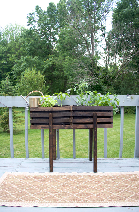 raised planter with herbs and watering can on a deck