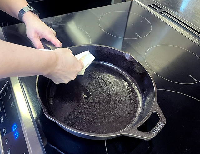 hand wiping oil into a cast iron pan to season it