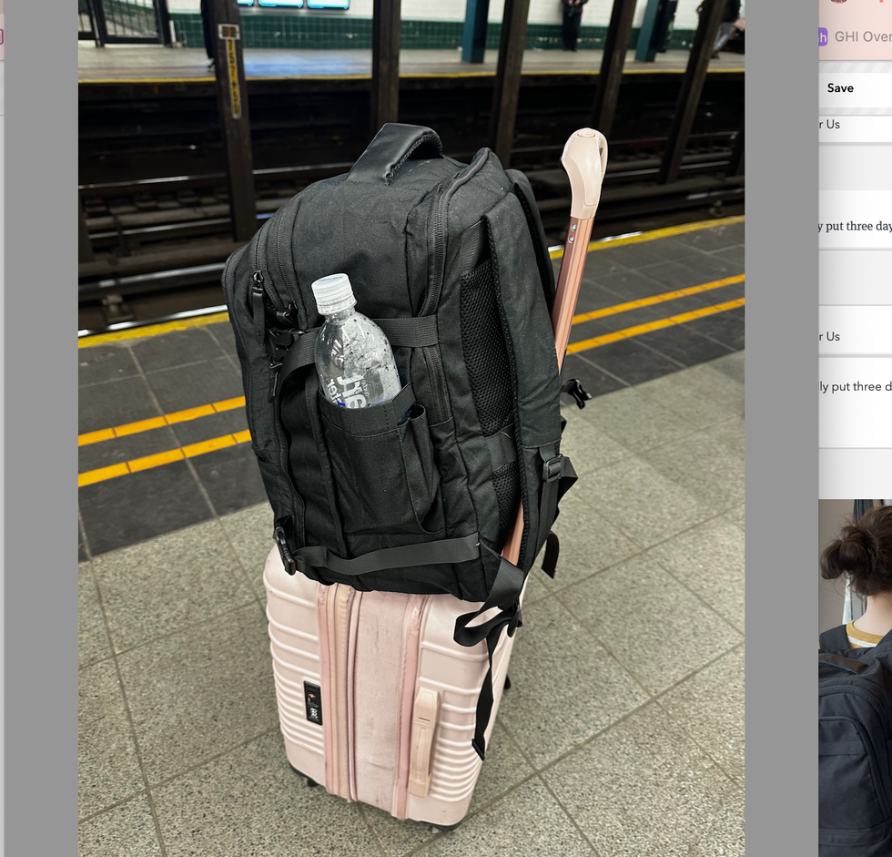 a black bagsmart backpack riding on top of a pink roller suitcase in the new york subway