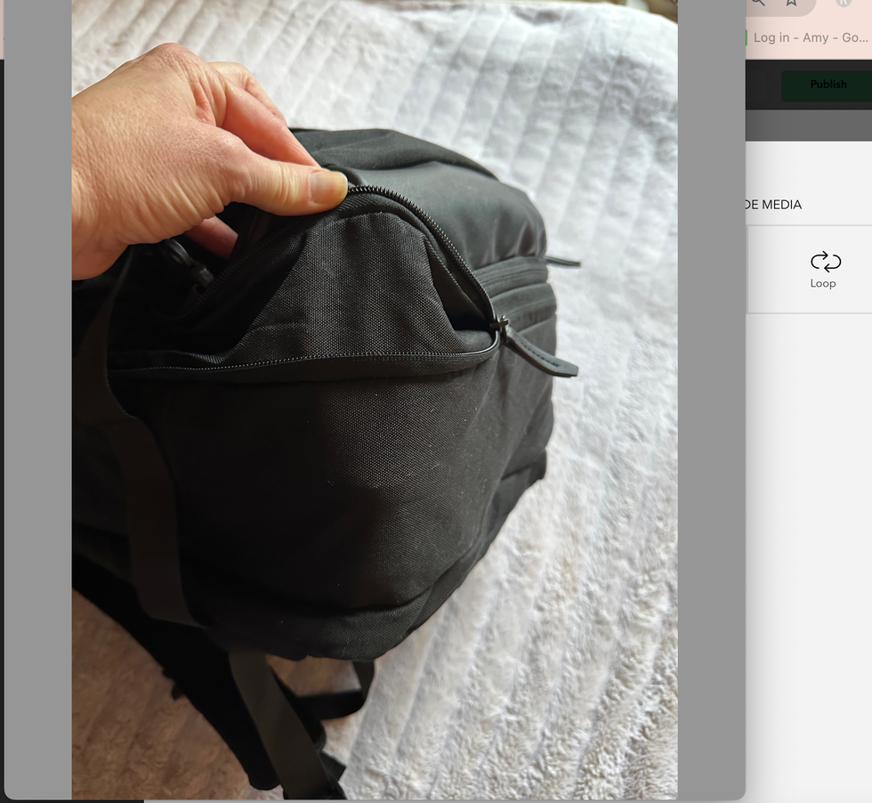 unzipping a black backpack on a bed