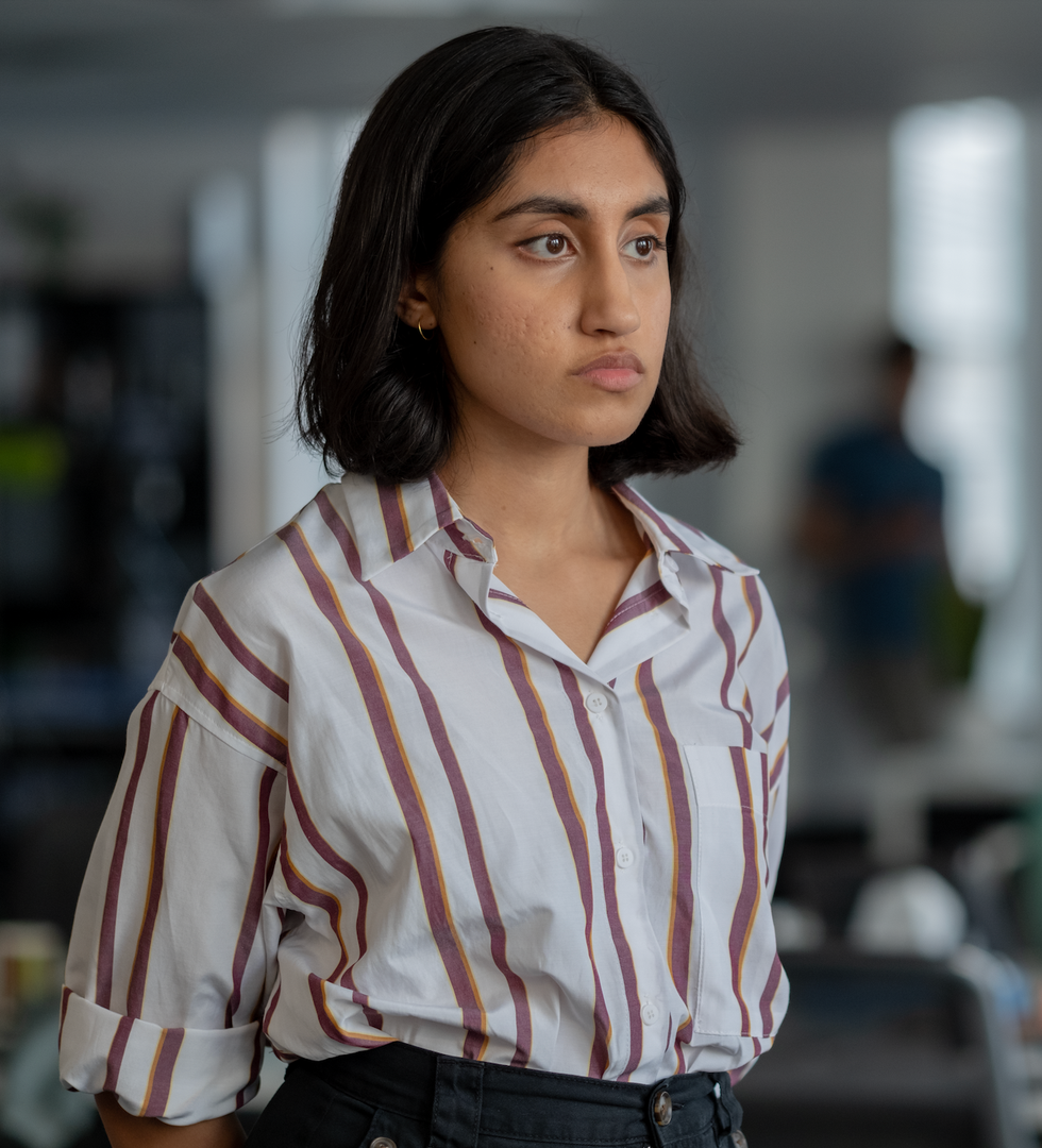 a person standing in an office setting wearing a striped shirt and dark pants