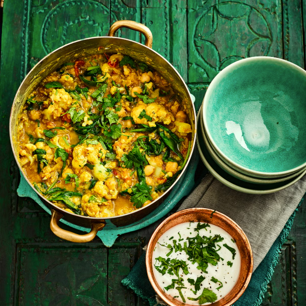 a vibrant dish of mixed vegetables and lentils in a pot accompanied by bowls and a yogurt side