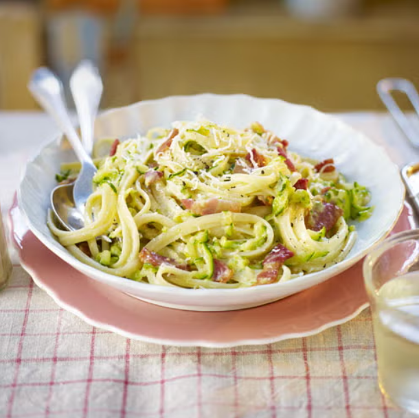 a plate of pasta with bacon and green vegetables garnished with cheese