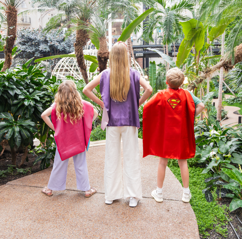 three children wearing colorful capes in a lush garden setting