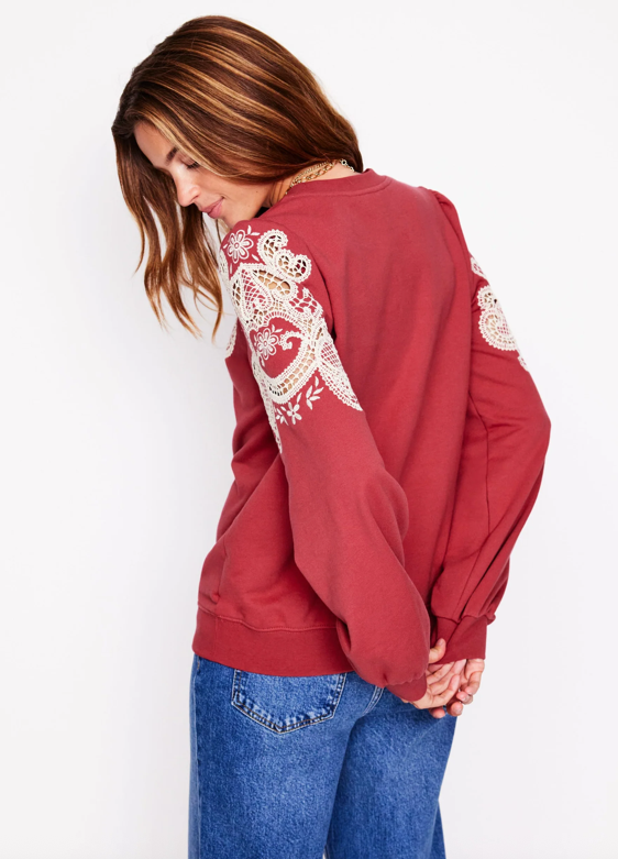 a casual outfit featuring a maroon sweater with ornate sleeve designs and denim jeans