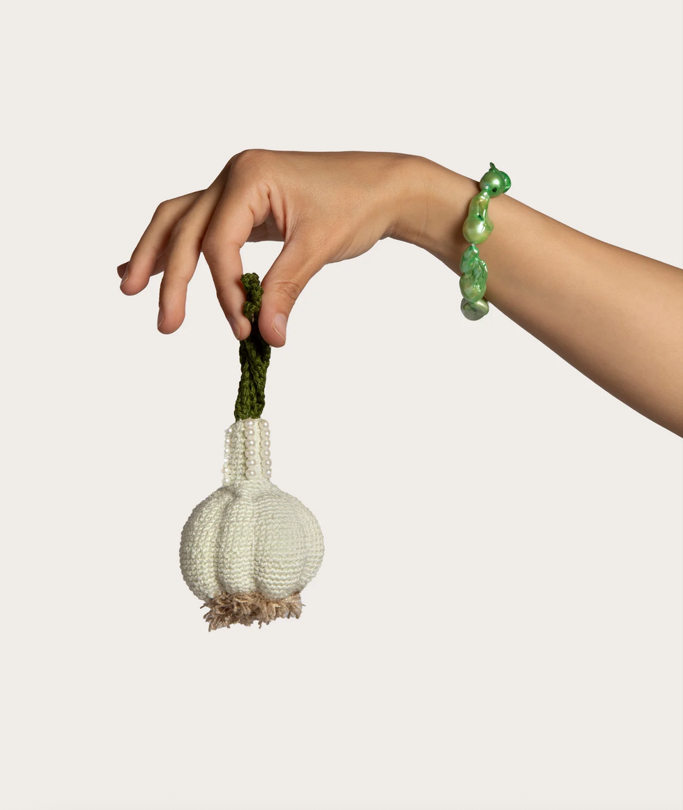 hand holding a crocheted garlic bulb with a decorative green stem and a pearllike accent