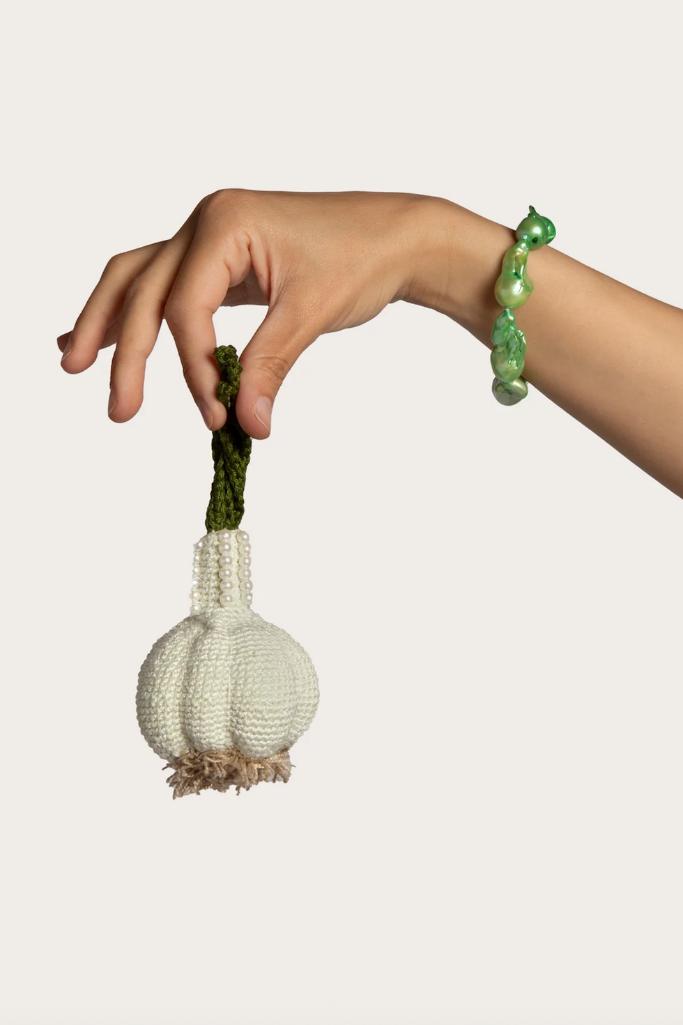 hand holding a crocheted garlic bulb with a decorative green stem and a pearllike accent