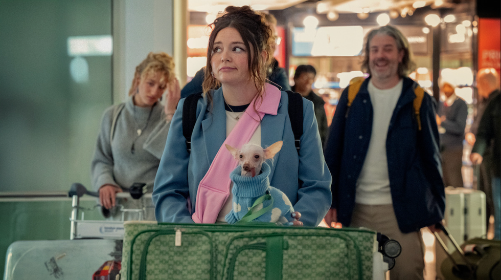 woman holding a small dog in a cozy outfit at an airport