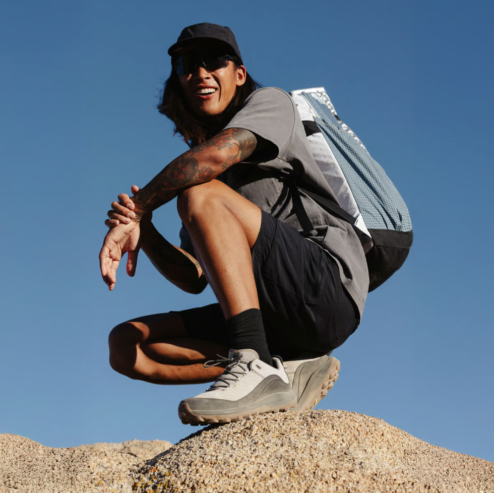 person crouching on a rock with a backpack and athletic shoes