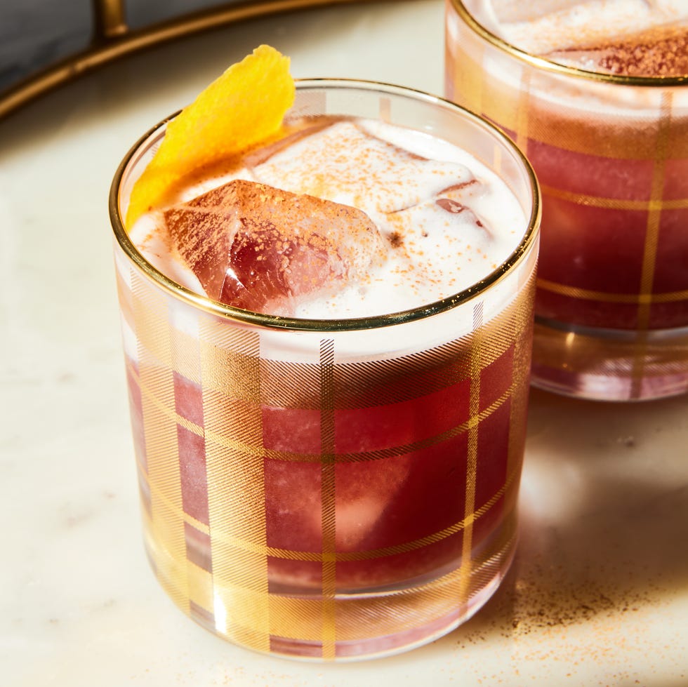 a red tinted sour garnished with an orange twist