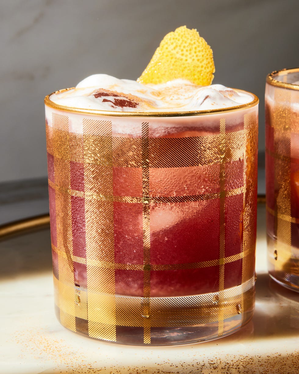a red tinted sour garnished with an orange twist