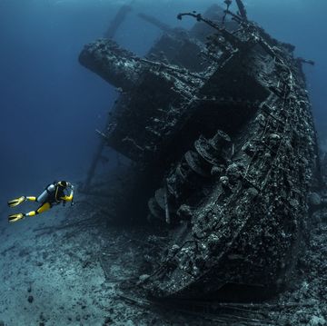 scuba diver observing a large shipwreck completely rusted and overgrown lying underwater in the red sea