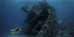 scuba diver observing a large shipwreck completely rusted and overgrown lying underwater in the red sea