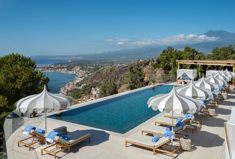 infinity pool overlooking a coastal landscape with lounge chairs and cabanas