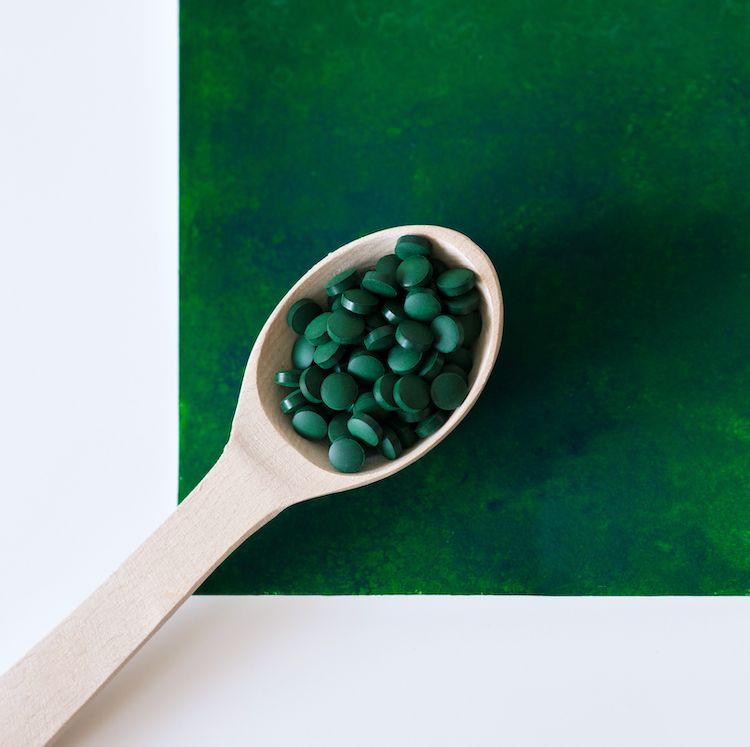 benefits of sea kelp green hawaiian spirulina in tablespoons pills in wooden spoon on green background super food, healthy lifestyle, healthy supplements, superfoods in cooking concept