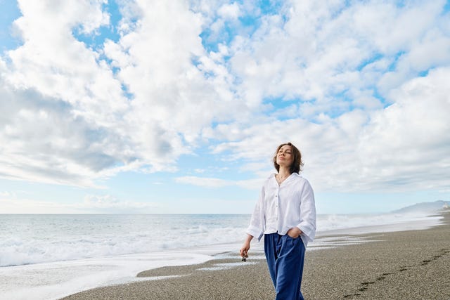 thoughtful woman with hand in pocket walking under cloudy sky