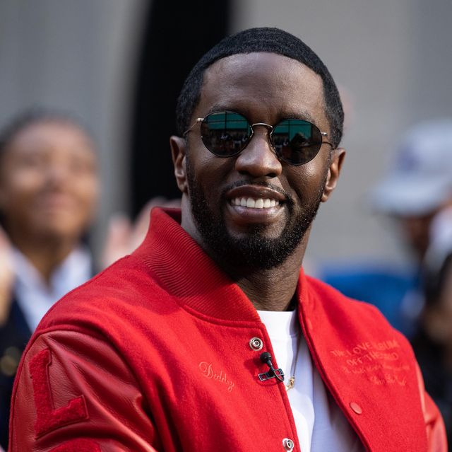 sean diddy combs smiles at the camera, he wears a red jacket over a white shirt and circular sunglasses