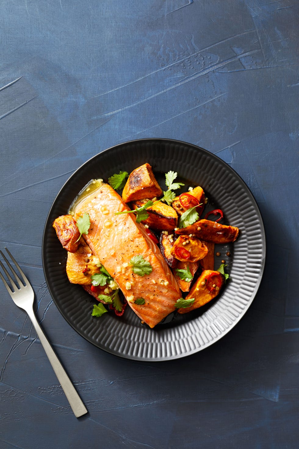 seared salmon with spiced sweet potatoes on black plate