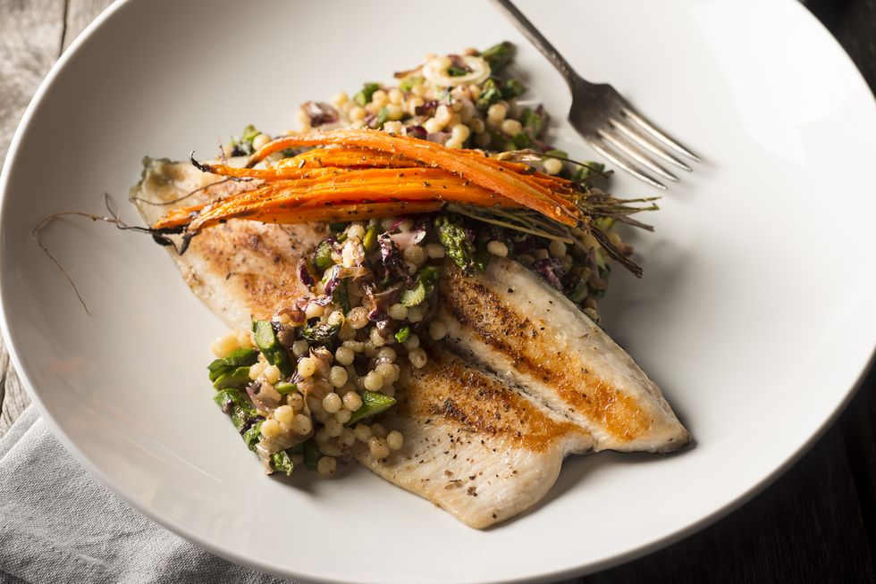 pan seared trout on a bed of grains, served on a white plate.