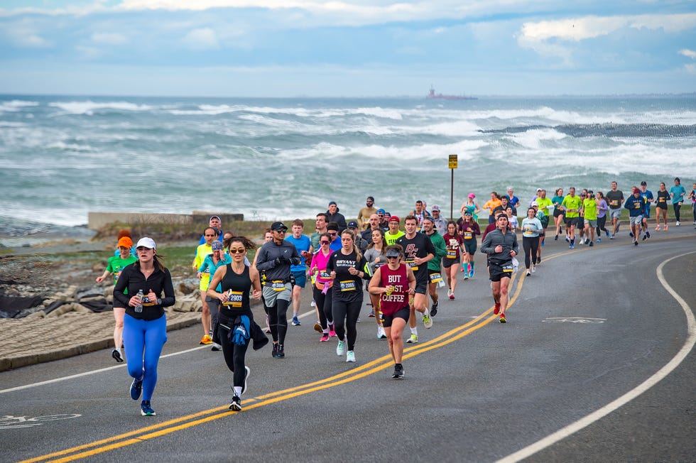 group of runners participating in a race alongside a coastal road at newport rhode race half marathon