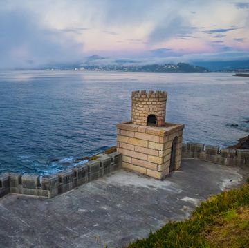 seascape at dusk with a small fortress and the town of bayona in background in galicia