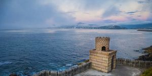 seascape at dusk with a small fortress and the town of bayona in background in galicia