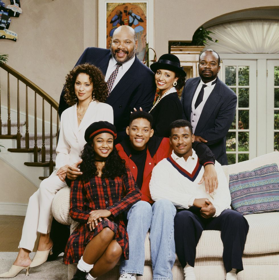 seven people pose for a photo around a couch, some sit and other stand behind, everyone smiles