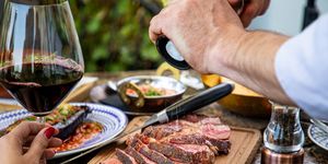 seasoning medium rare steak with salt grinder, cut on wooden board on restaurant table