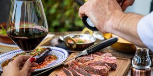 seasoning medium rare steak with salt grinder, cut on wooden board on restaurant table
