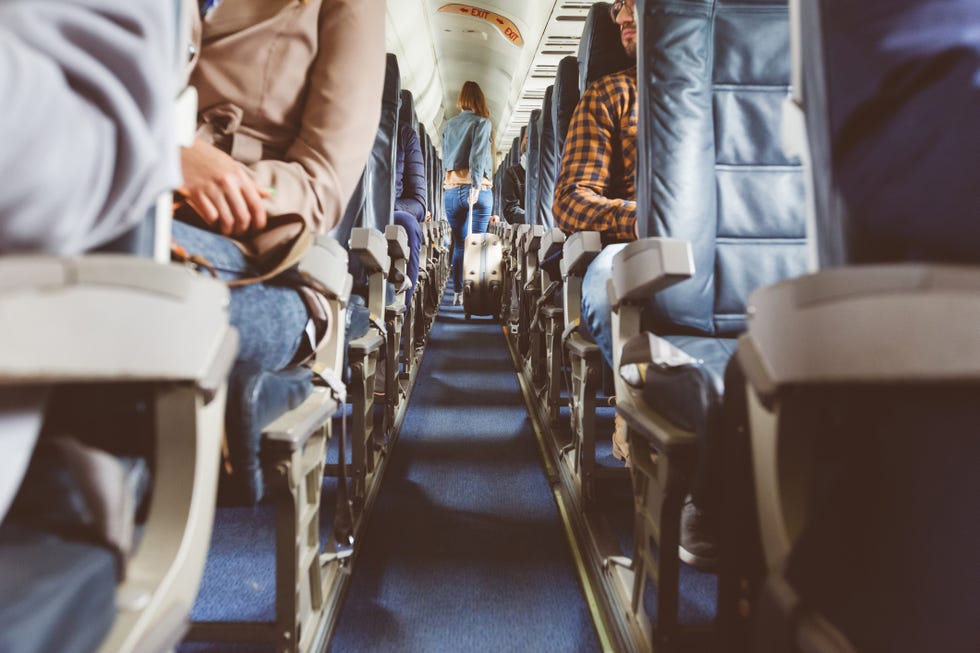 interior of airplane with people sitting on seats. passengers with suitcase in aisle looking for seat during flight.