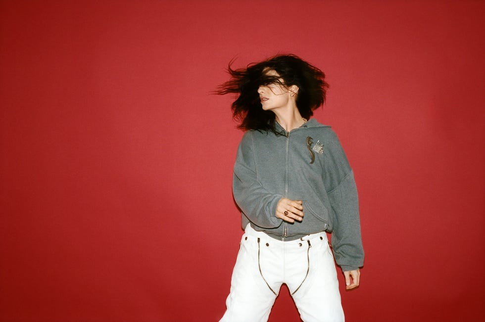 person in casual attire dancing in front of a red background