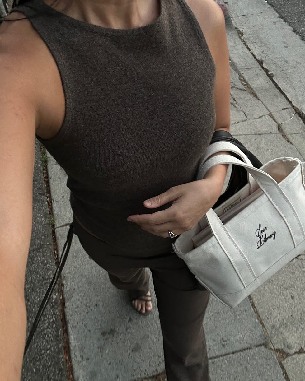 a woman walking on the street with a seen library mini tote bag on her wrist