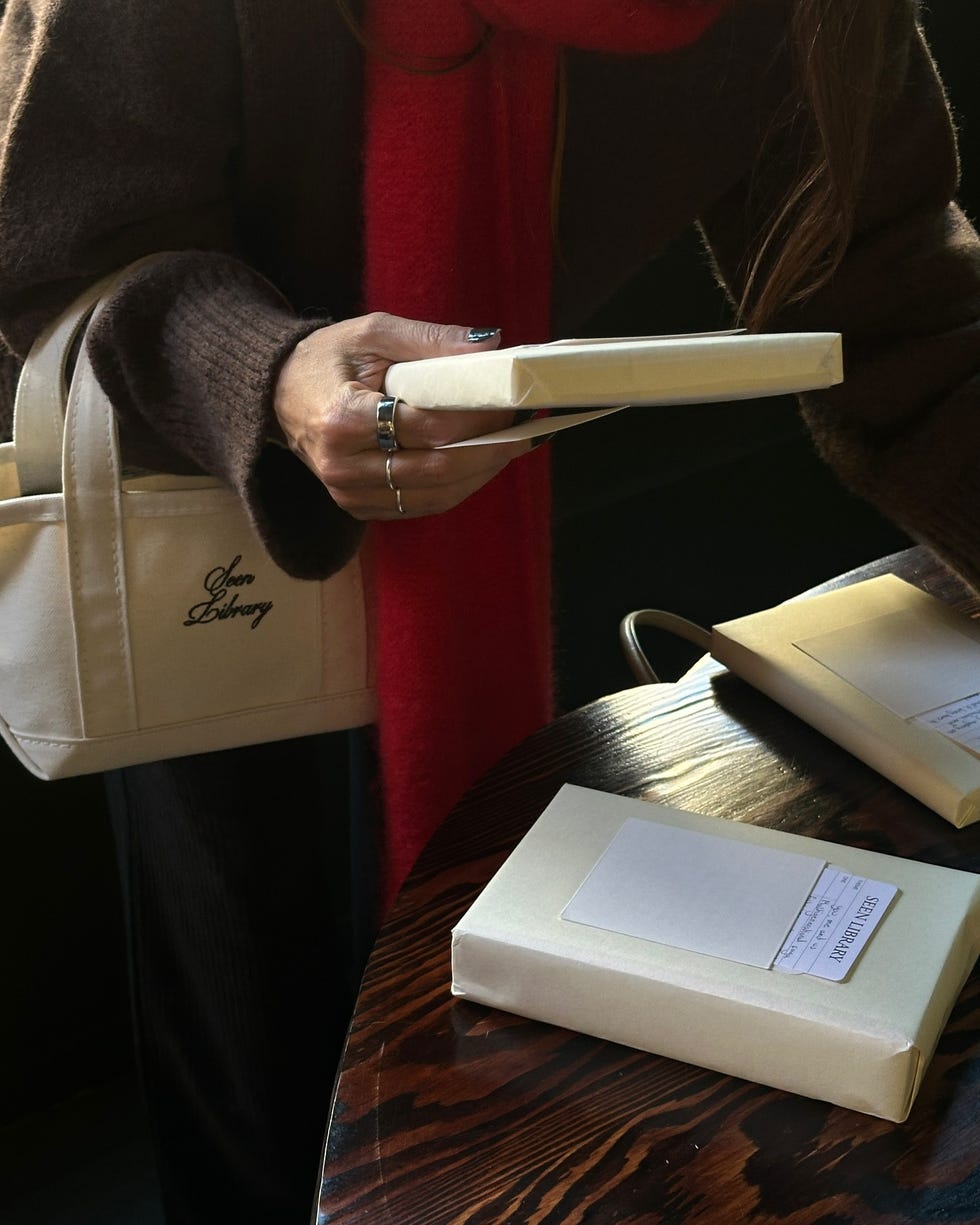 a woman looking at books while holding a seen library mini tote bag on her wrist