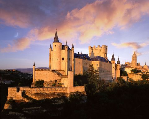 Zoals de meeste Spaanse kastelen werd het fort van Segovia ter verdediging van de stad gebouwd maar van de oorspronkelijke vesting is maar weinig bewaard gebleven De ronde torens die nu hoog boven de samenloop van twee rivieren oprijzen doen meer denken aan een sprookjeskasteel dan een fort Het indrukwekkende stenen bouwwerk heeft talloze functies gehad waaronder die van koninklijk paleis koningin Isabella I werd hier in 1474 gekroond staatsgevangenis en militaire academie Tegenwoordig is het kasteel een prachtig museum met vergulde zalen topschilderijen meubels en wapens In 1967 diende het slot als huis van Sir Lancelot in de Hollywoodfilm Camelot