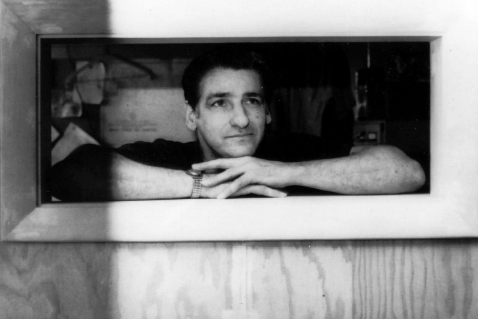 albert desalvo stands and peers through a small window, his arms are resting on the sill and he is wearing a watch