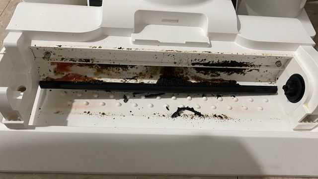 a white vacuum nozzle showing red and black debris after self clean function was run on a vacuum mop