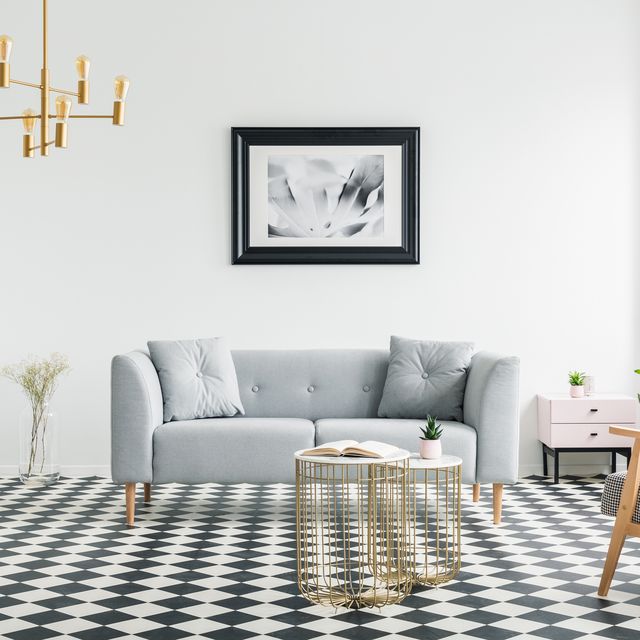 Poster above grey sofa in bright patterned living room interior with armchair and gold lamp. Real photo