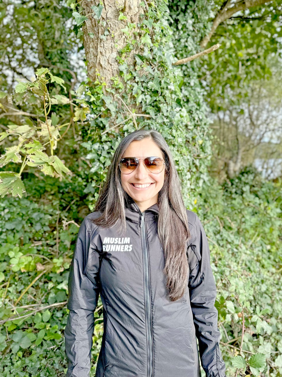 smiling woman standing beside a tree in a muslim runners jacket