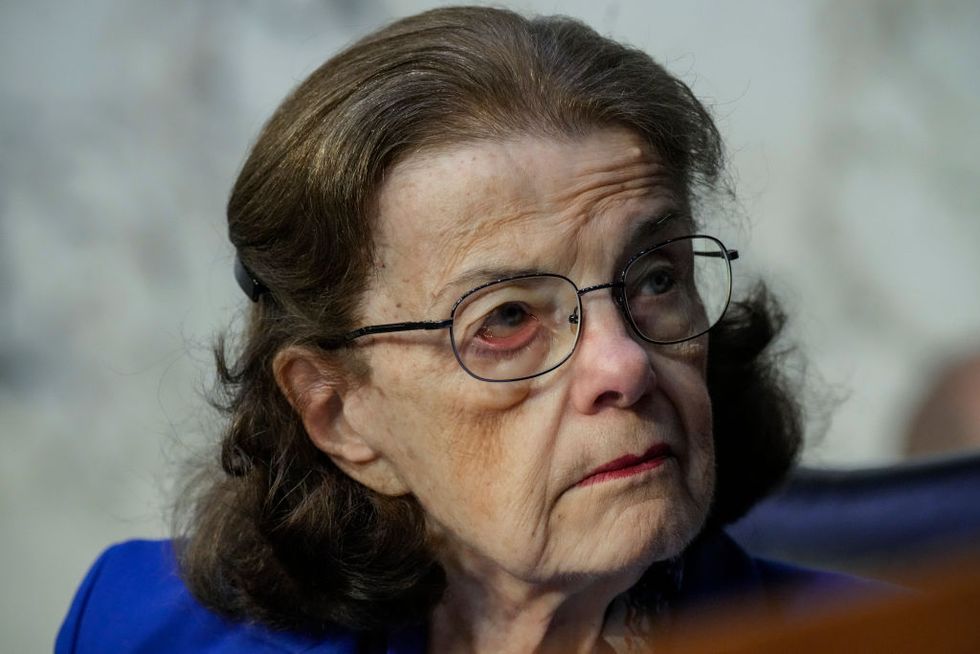 dianne feinstein, wearing a blue outfit and glasses, looks off camera and listens to someone