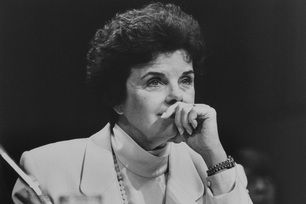 a black and white photo of dianne feinstein sitting and listening to something, with her hand on her mouth