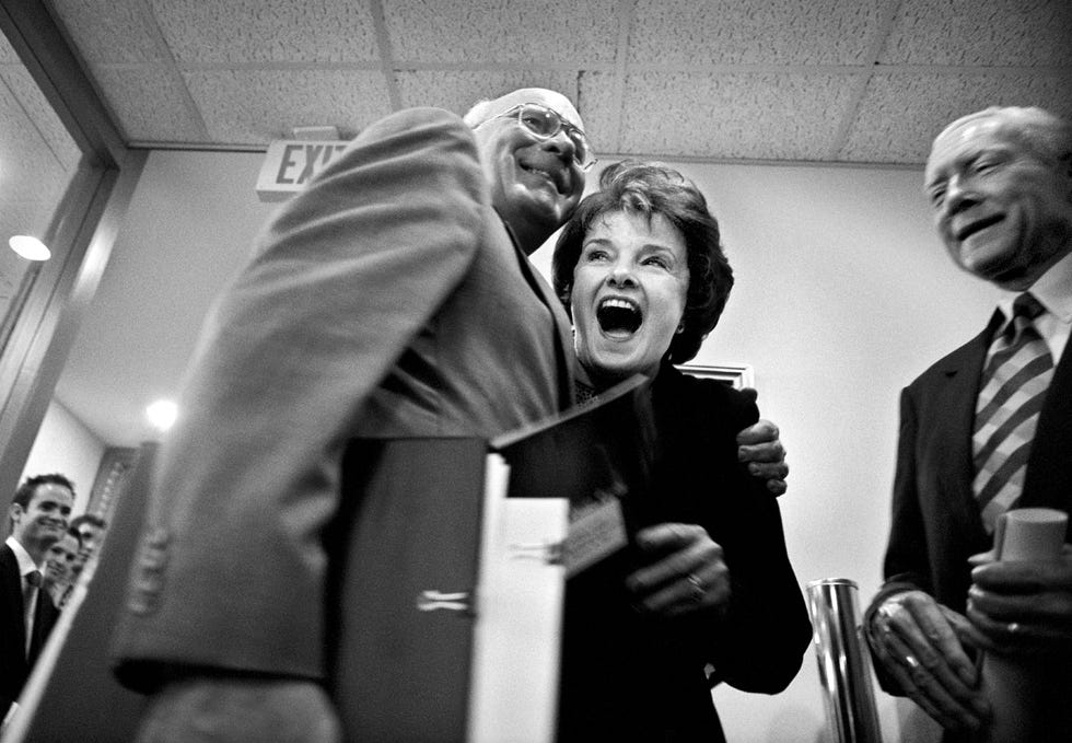 patrick leahy hugging a laughing dianne feinstein as both hold binders, with orrin hatch standing next to them and smiling
