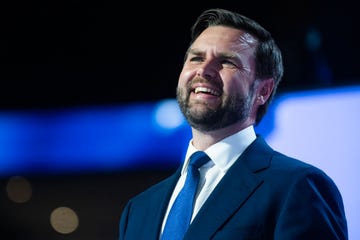 jd vance looking up and smiling, he wears a navy suit jacket, white collared shirt and a blue tie