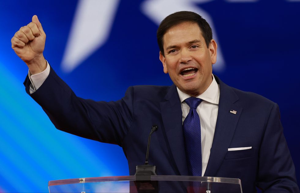 marco rubio raising and making a fist with his right arm as he speaks behind a glass podium