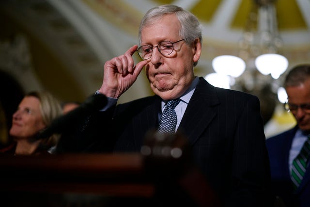 mitch mcconnell adjusts his glasses while standing at a podium