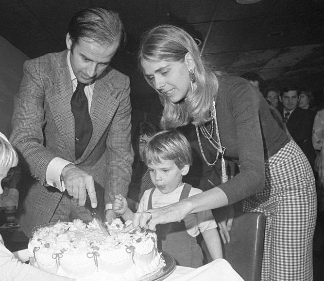 a black and white photo of joe and nelia biden cutting a piece of cake while hunter biden looks on and another child stands near the table