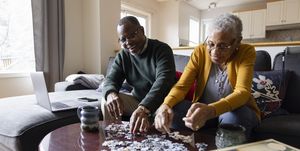 senior couple assembling jigsaw puzzle on living room coffee table