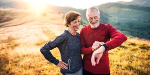 senior couple runners resting outdoors in nature at sunrise, using smart watch